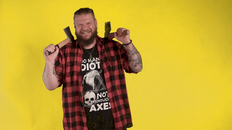 A tattooed presenter holding two axes against a yellow backdrop, from our film for Wellbe