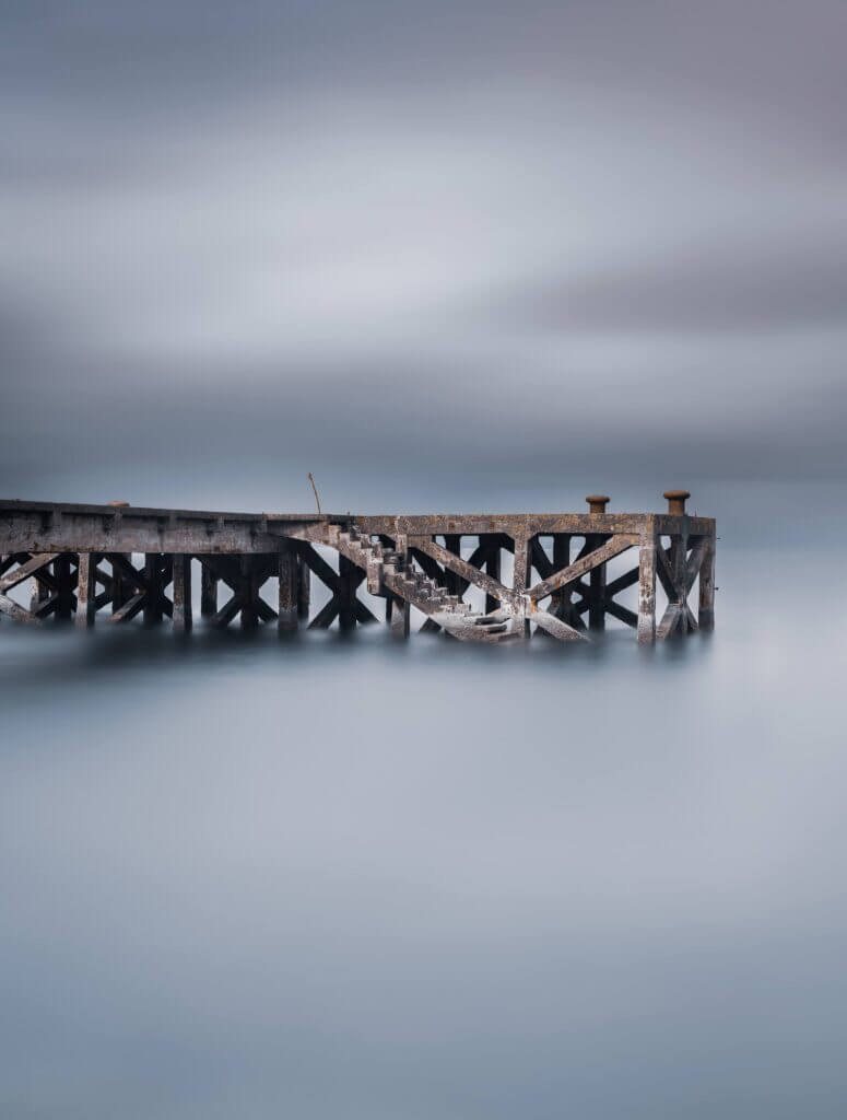 Old posts in misty, still water, photographed by David Barco