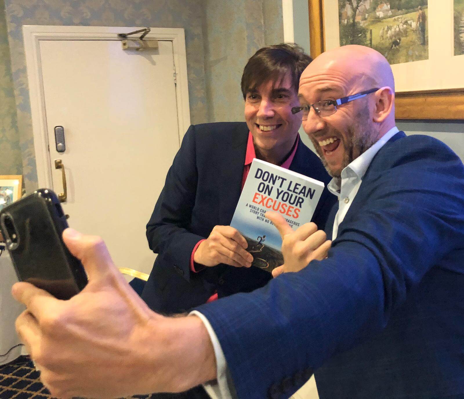 Steve holding a copy of his book with a guest taking a selfie